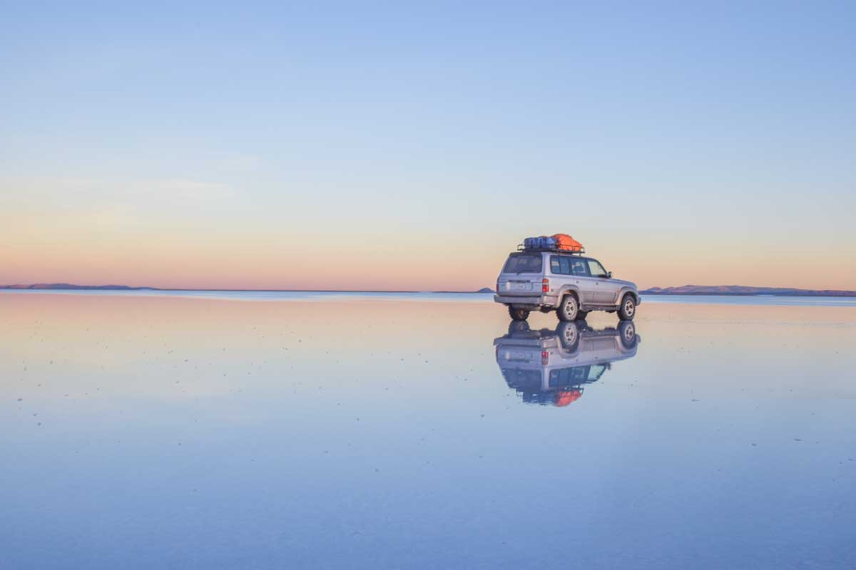 A 4wd at sunset on the reflective plains of the Uyuni Salt Flat while water is still on the ground