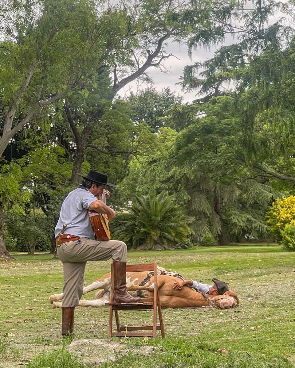 Man lays down with his horse while a Gaucho plays music to the horse