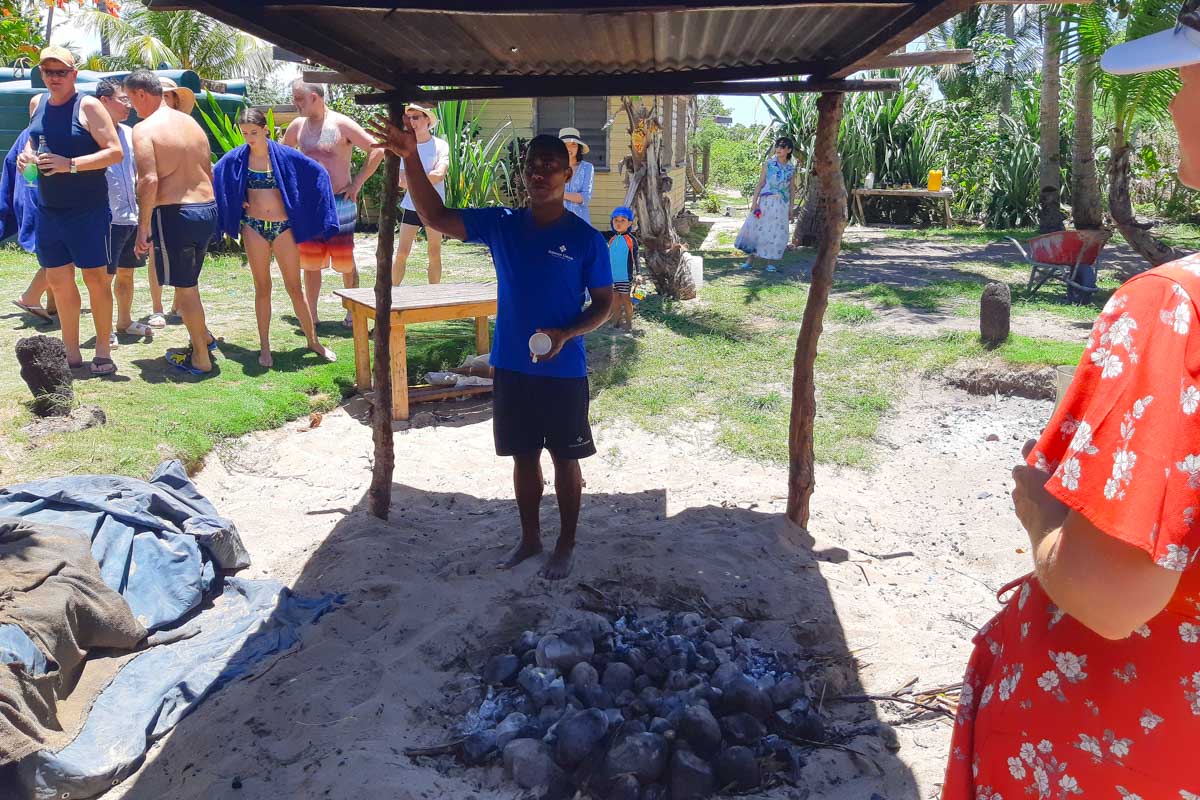 A fijian man gives a demonstration in a covered area by a fire pit on robinson crusoe island fiji