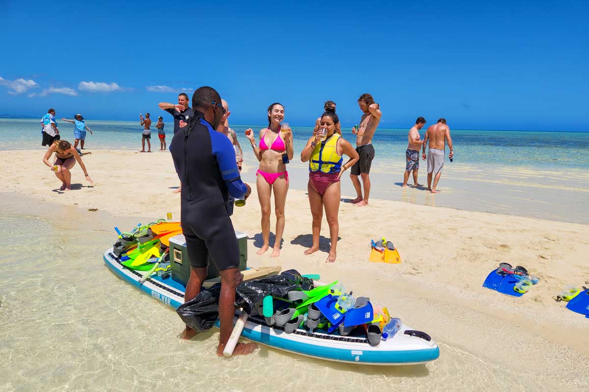 A local Fijian talking to two women and handing out snorkeling gear on a sand bar Fiji