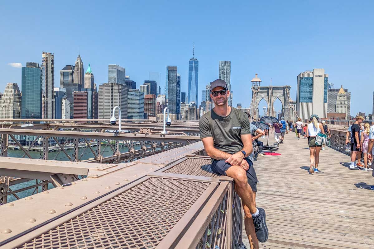 Daniel sits on the railing of the Brooklyn Bridge walkway and poses for a photo