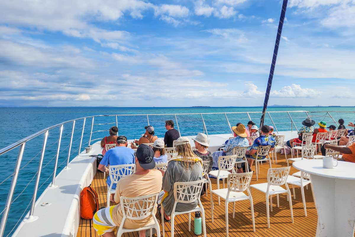 People sit on the outdoor deck of the boat to Tivua Island in Fiji