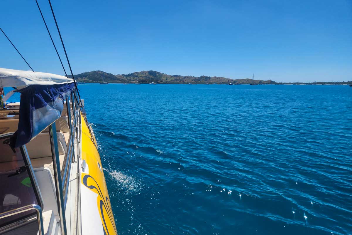 Sailing towards an island and looking at the turquise blue water from the deck of the Sabre catamaran Fiji