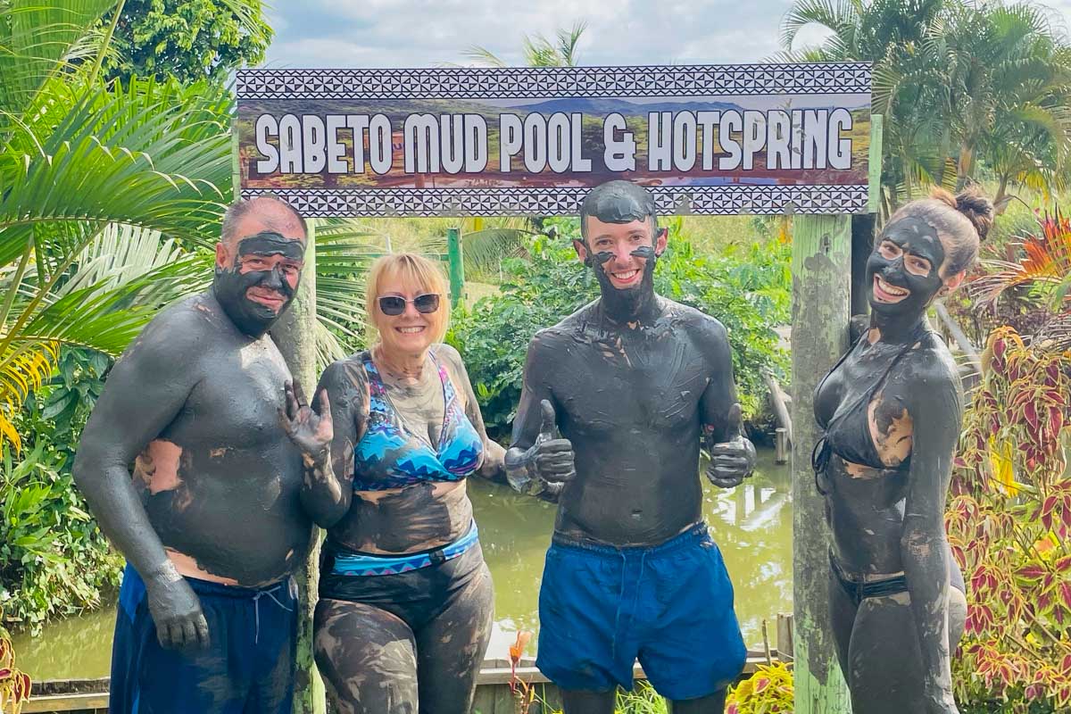 A group of people smiling in front of the Sabeto hot springs and mud pool sign fiji