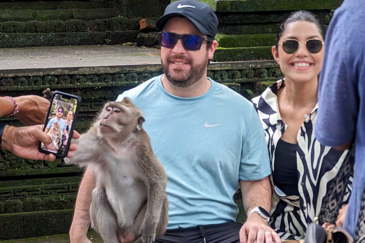 A man and woman pose with a monkey for a picture at Ubud Monkey Forest Bali