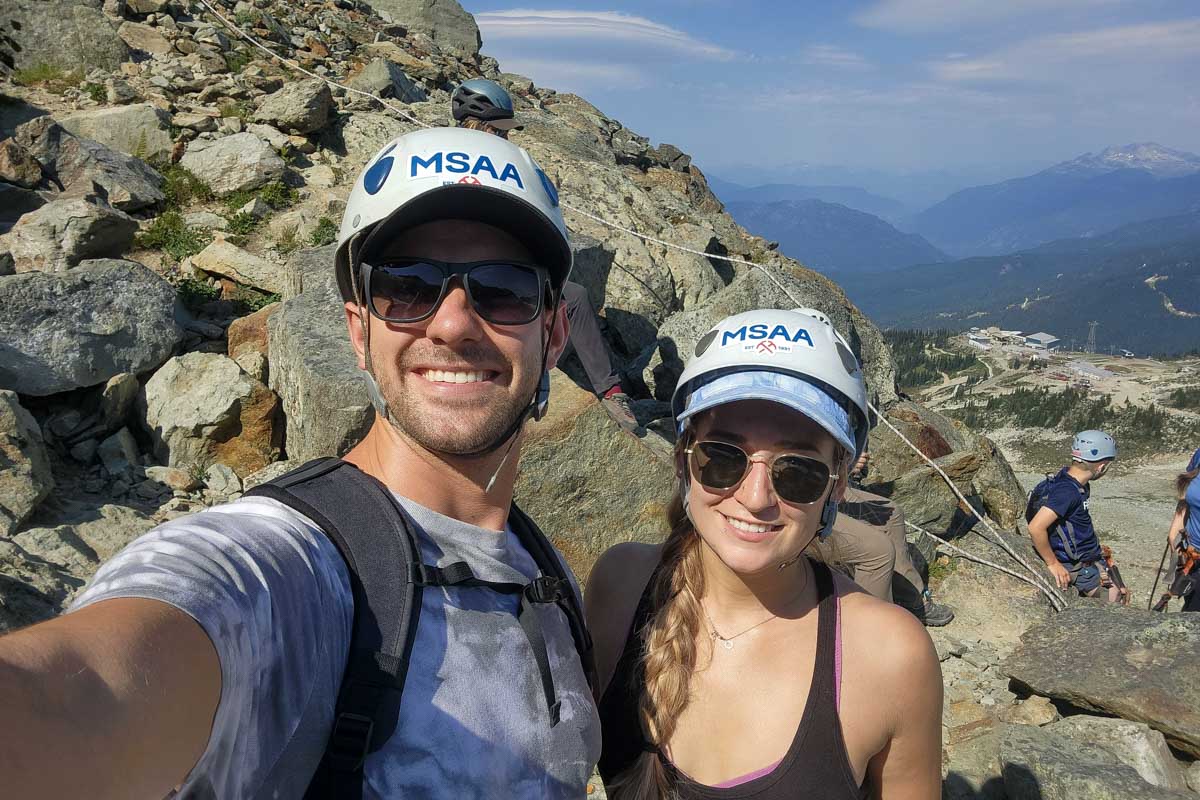 Bailey and Dan smile for a selfie with the rockies behind them during Via Ferrata, Whistler, Canada