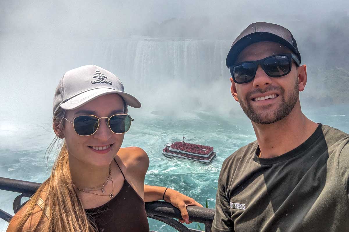 Bailey and Daniel take a selfie with a tour boat behind them niagara falls canada