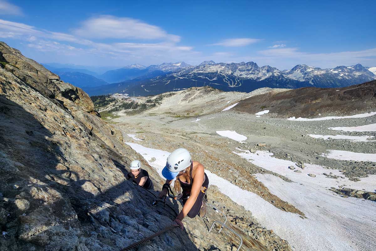 Bailey and another person climb with the rockies behind them during Via Ferrata, Whistler, Canada