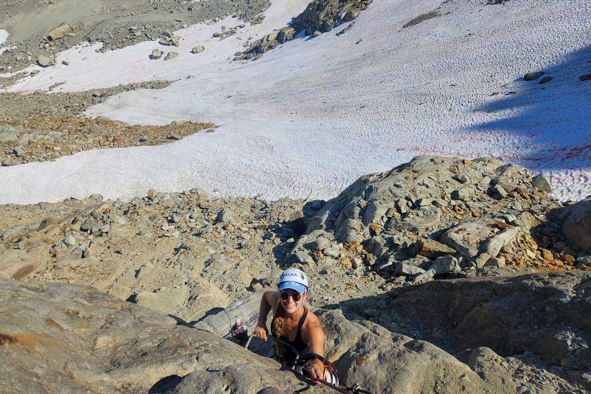 Bailey climbing rocks with a snow field behind her during Via Ferrata, Whistler, Canada