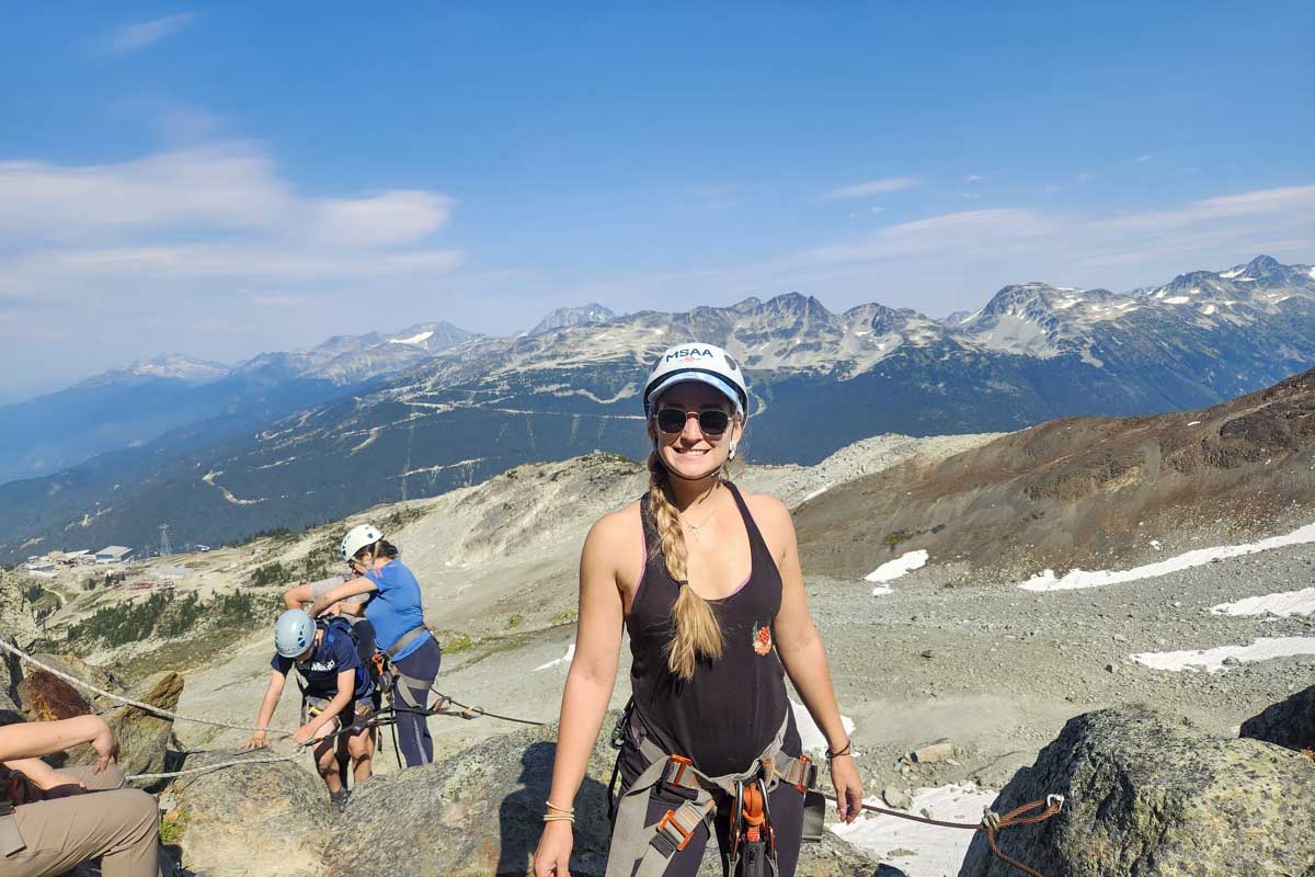 Bailey poses and smiles with the rockies behind her during Via Ferrata, Whistler, Canada