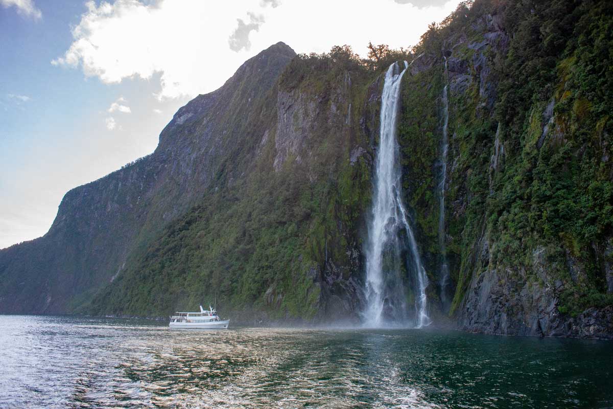 A boat getting close to a waterfall on the milford sound nature cruise new zealand