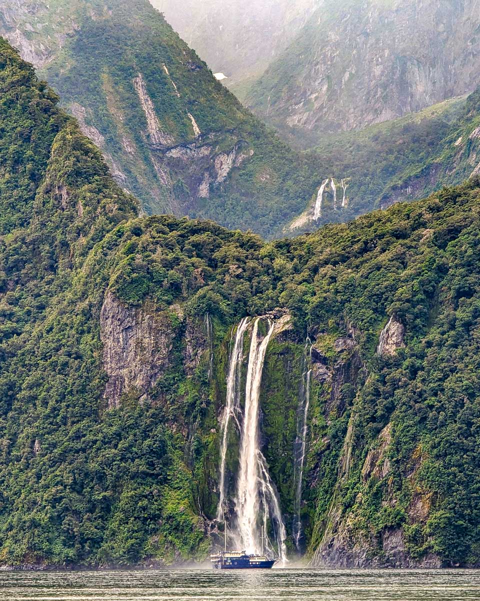 A boat near a big waterfall on a Milford Sound cruise New Zealand