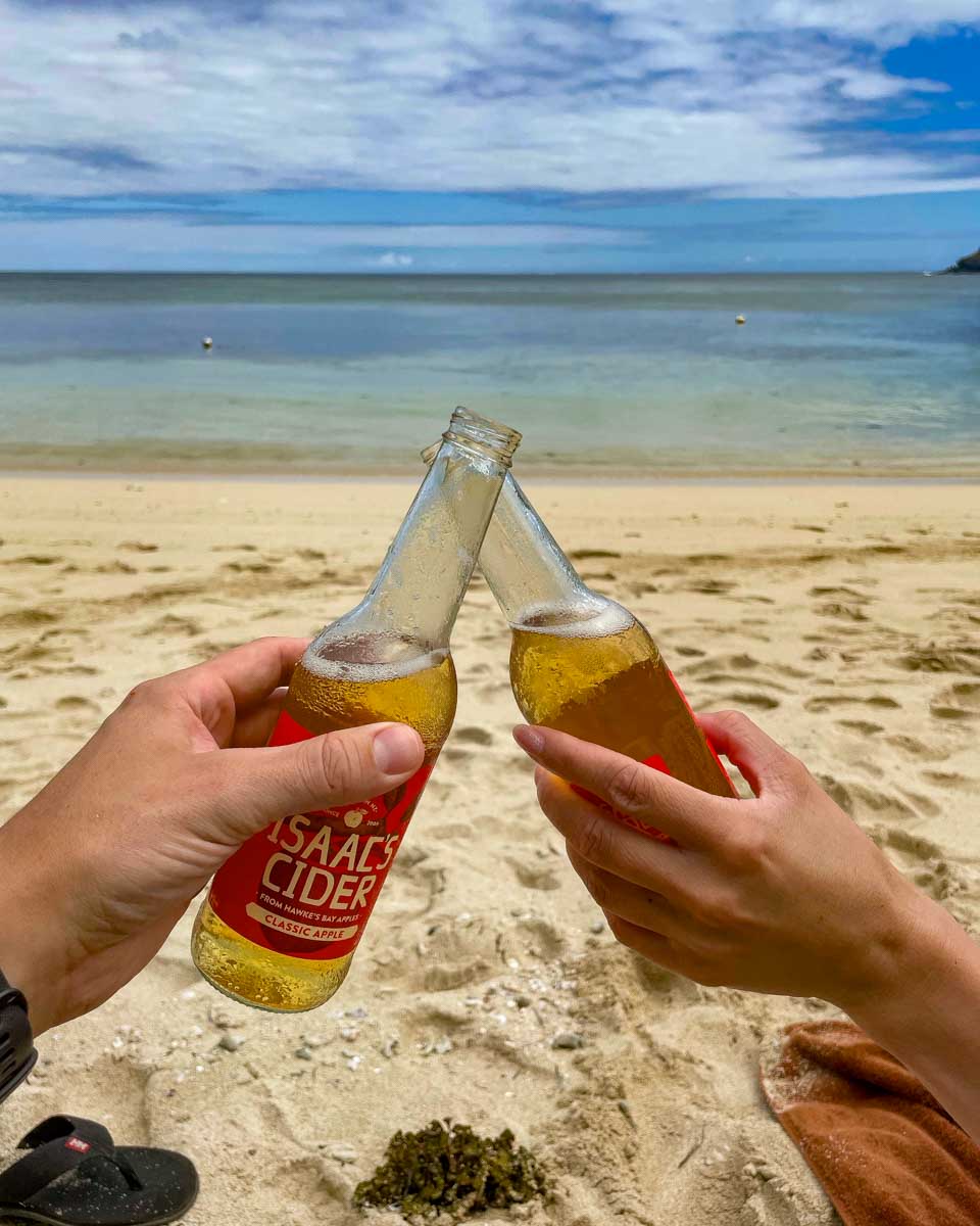Two people drink cider on the beach in Fiji on a multi day cruise