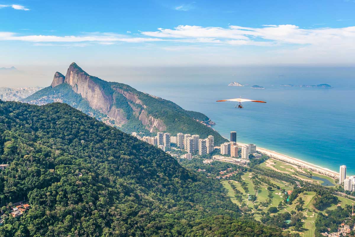 a person hang glides in Rio with mountains, city, and ocean in the background