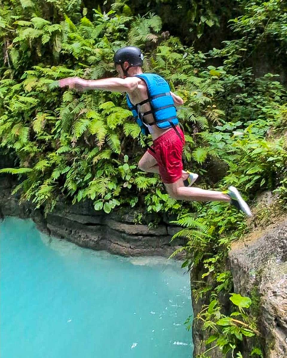 PH Kawasan Canyoneering a man jumps off of a cliff while on a tour from Cebu Philippines