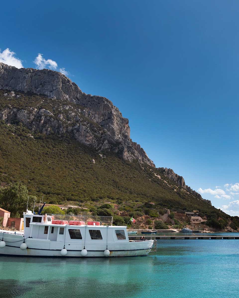 A boat floating on turquoise water with Tavolara Cliff in the background seen on a boat tour in Sardinia Italy