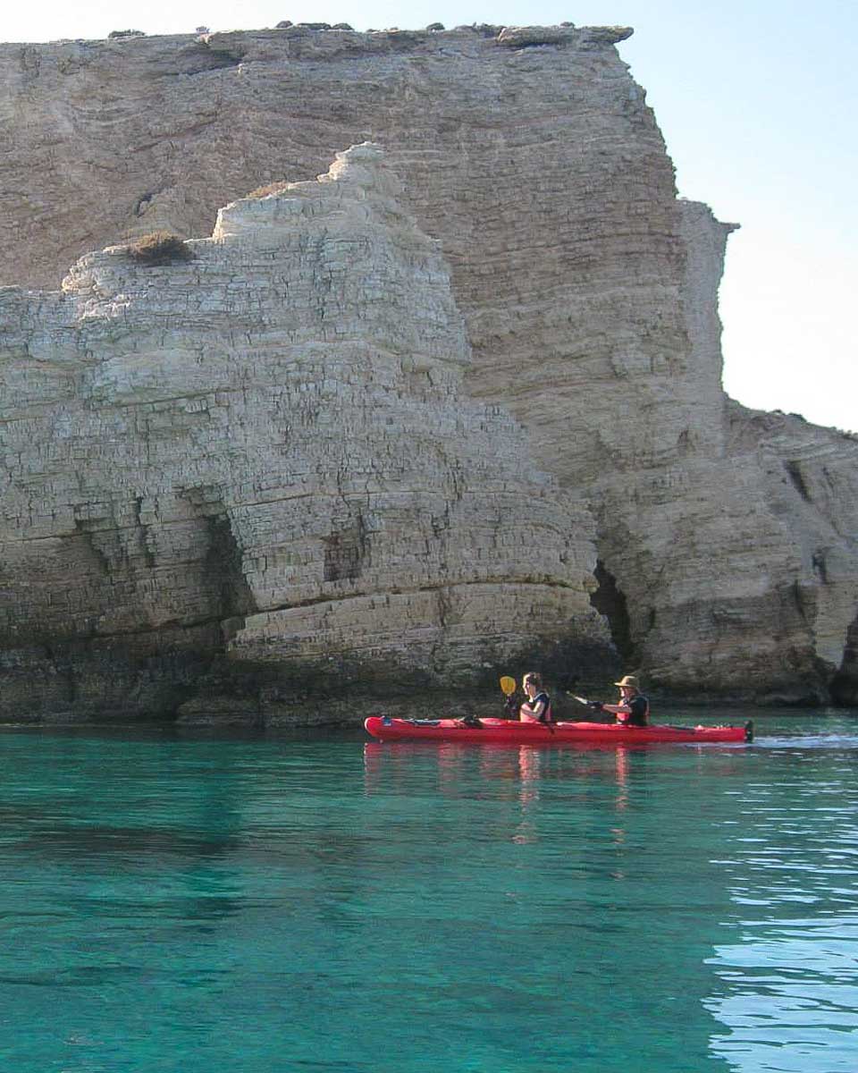 A kayak passes by dramatic sea cliffs on a tour in Santorini Greece