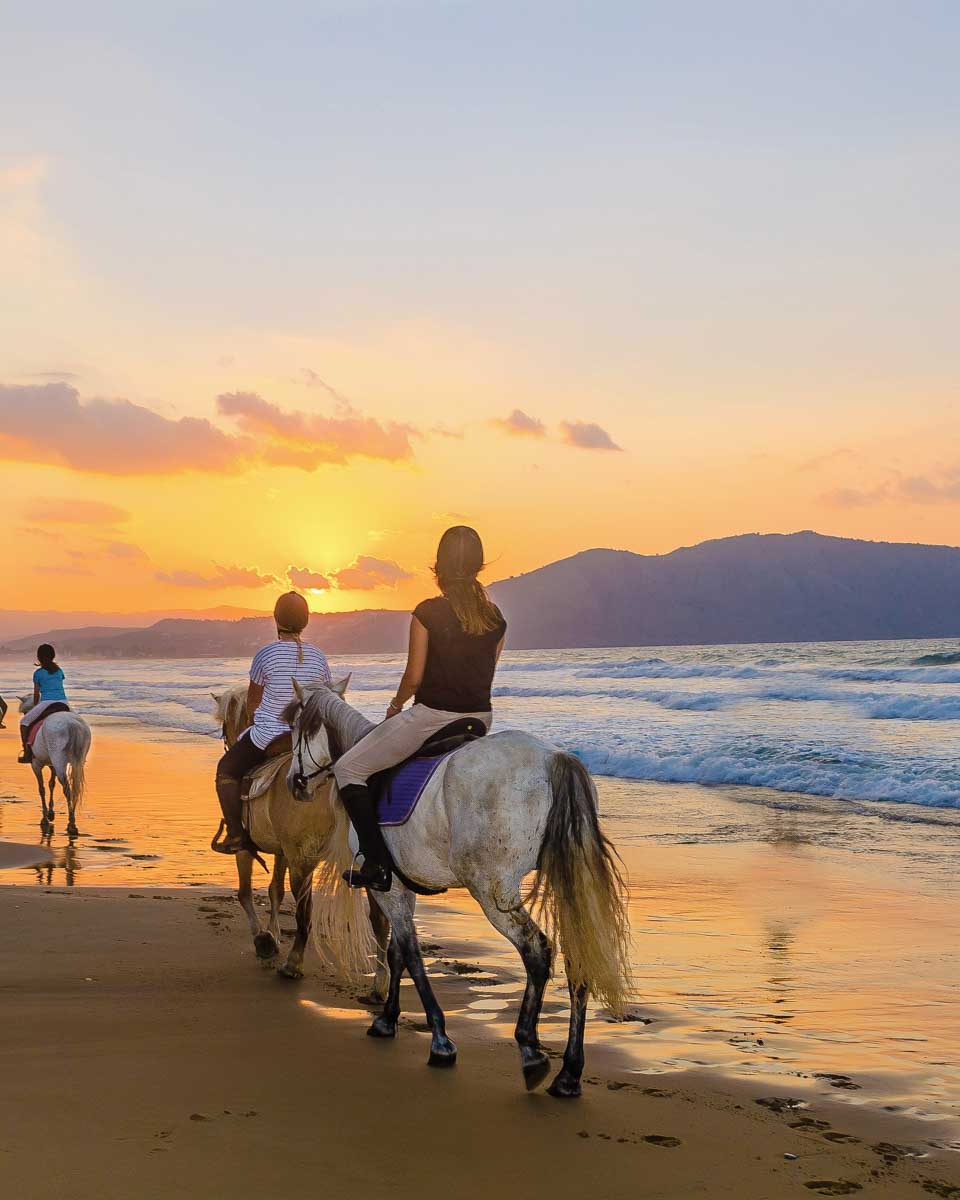 A sunset and people riding horses on the beach on a tour in Santorini Greece