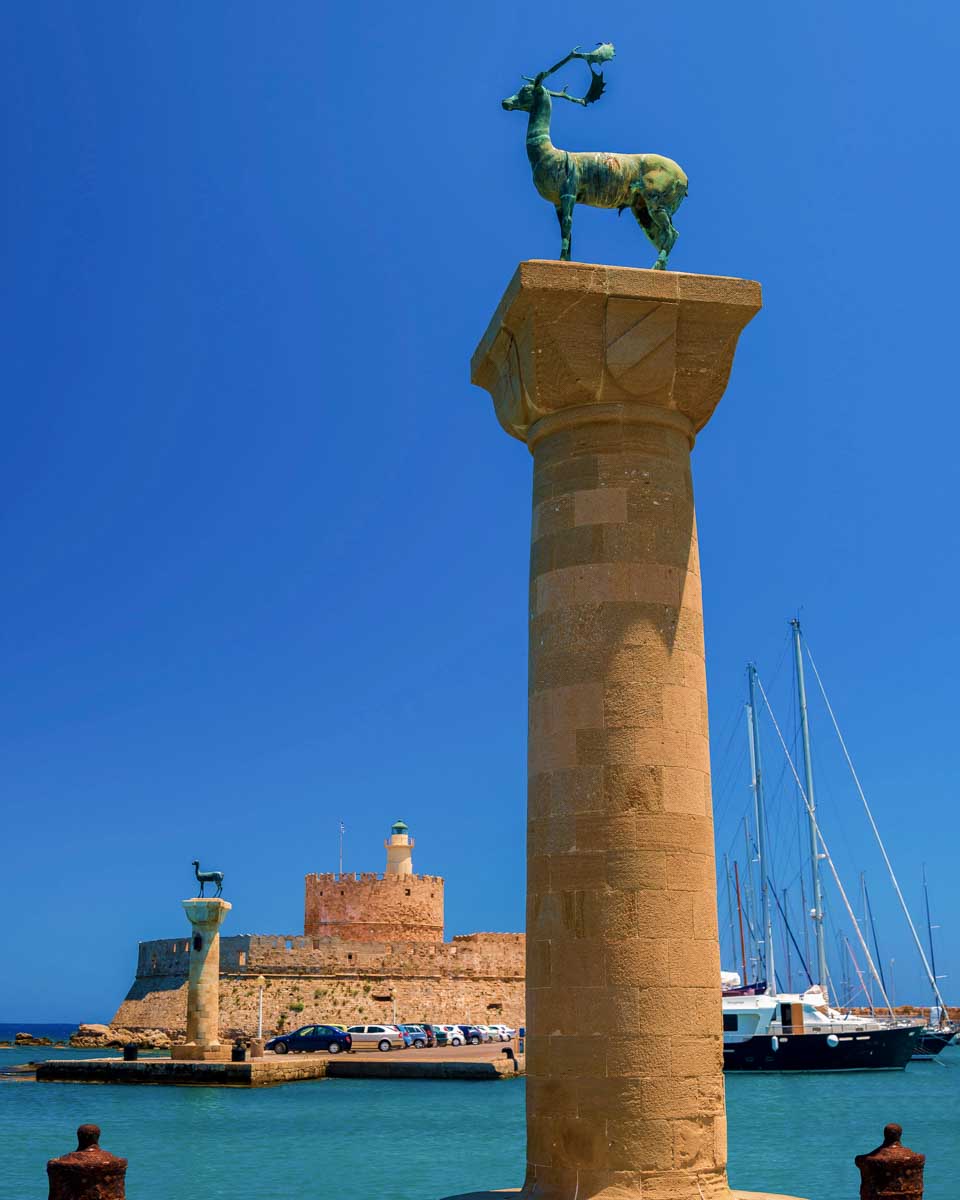 Statues stand either side of Mandraki harbour entrance where colossus of rhodes stood Rhodes Greece