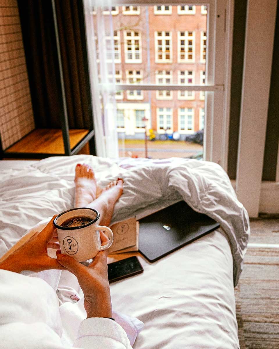 A lady enjoys coffee in bed looking out the window at Mr Jordaan Hotel in Amsterdam