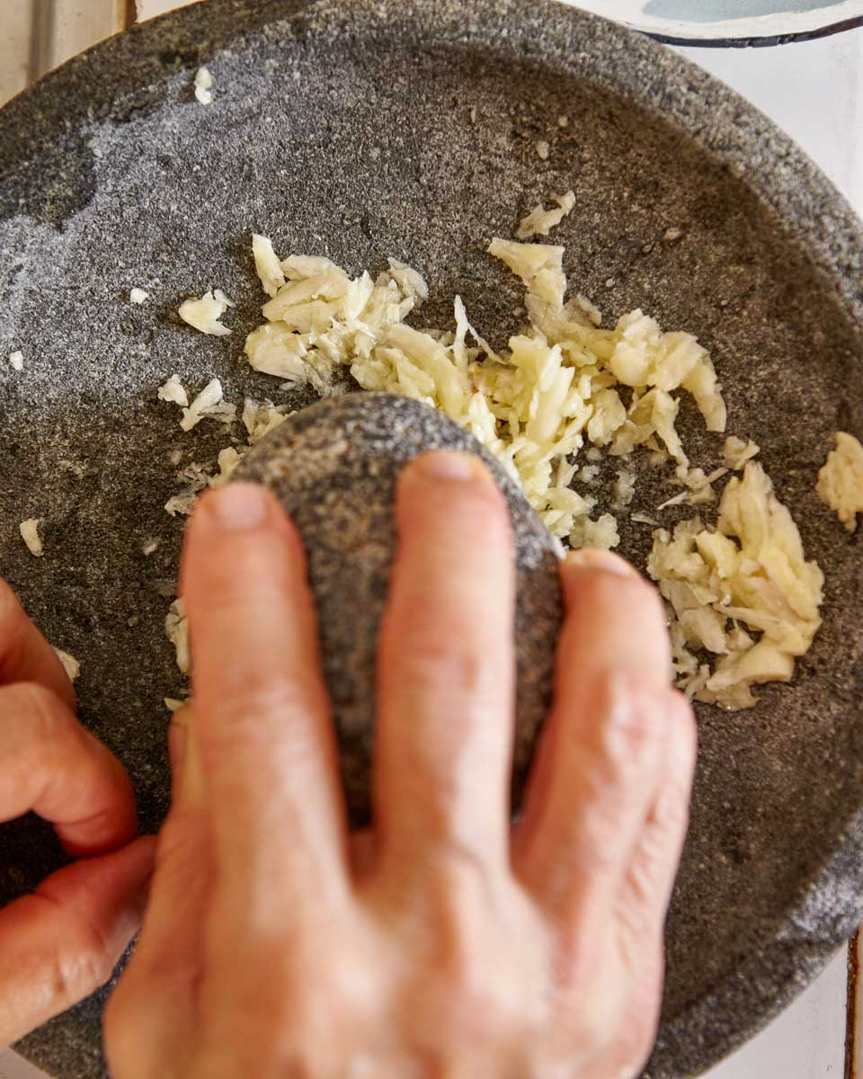 A-person-grinds-up-garlic-in-a-stone-bowl-making-pesto-during-a-cooking-class-in-Cinque Terre Italy