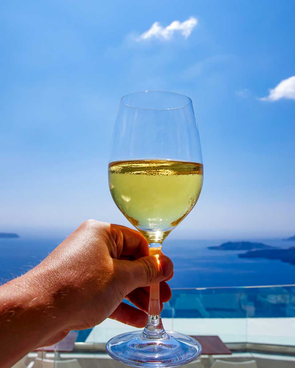 A person holds a glass of wine with the Aegean Sea in the background on a tour from Santorini Greece